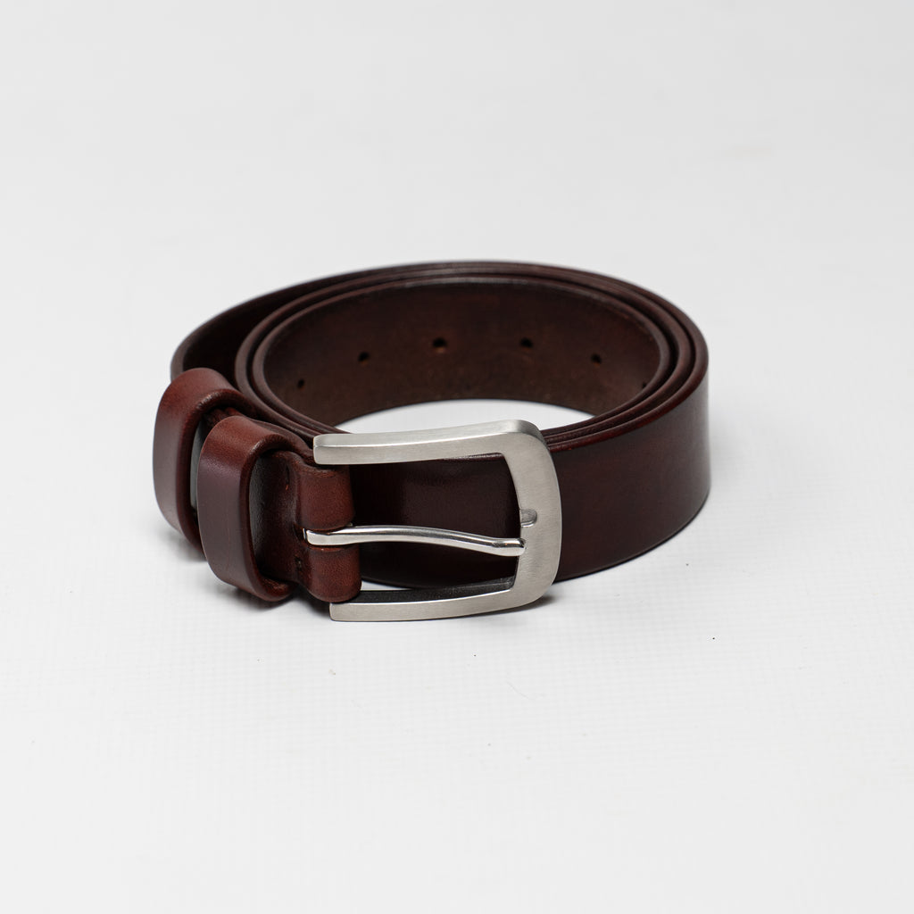 A mahogany hand dyed leather belt with a stainless steel buckle, neatly coiled on a light gray background. Made by Atom Leather