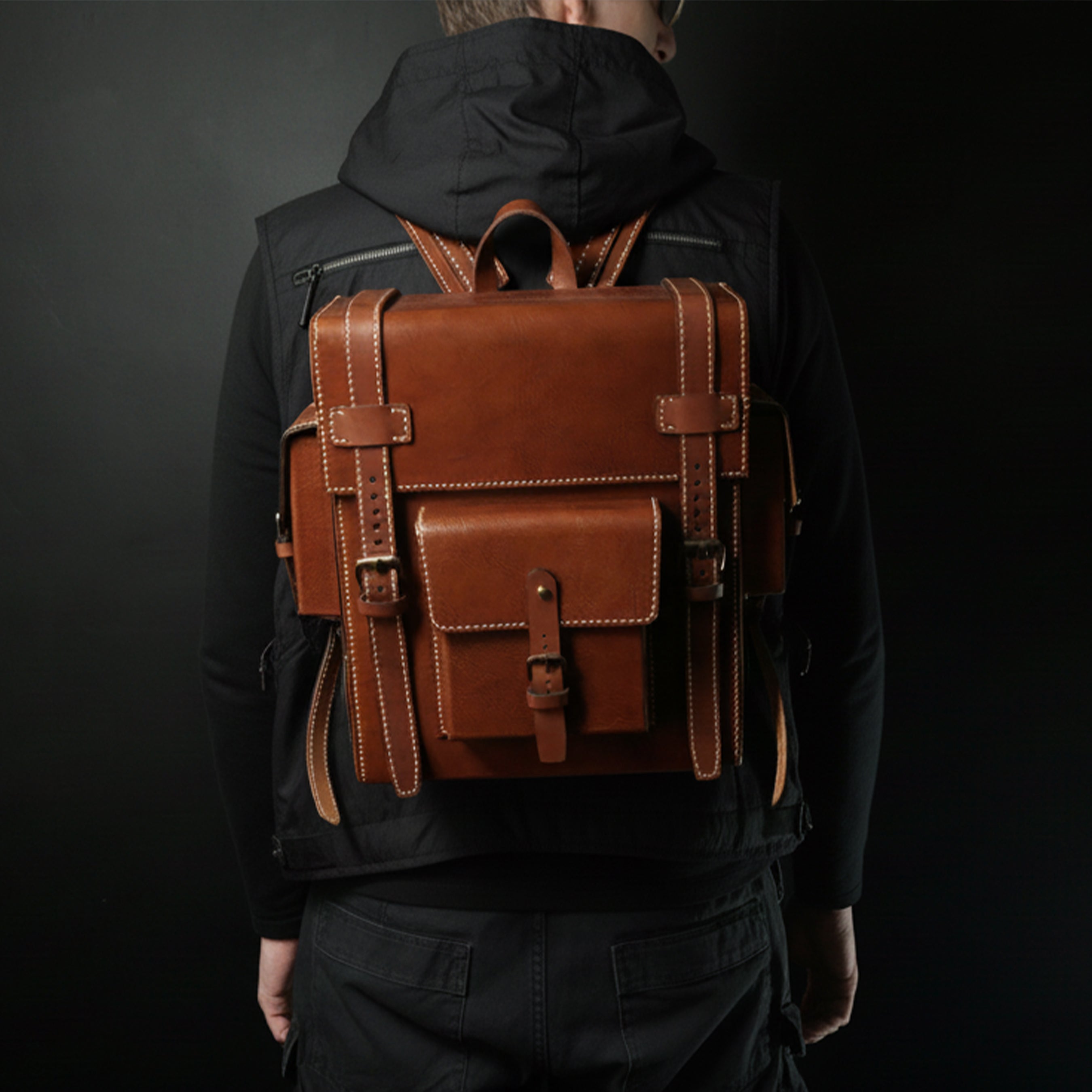 Person wearing a brown leather backpack against a black background. Brown leather Toshiro backpack on a white background, designed and handcrafted by ATOM LEATHER.