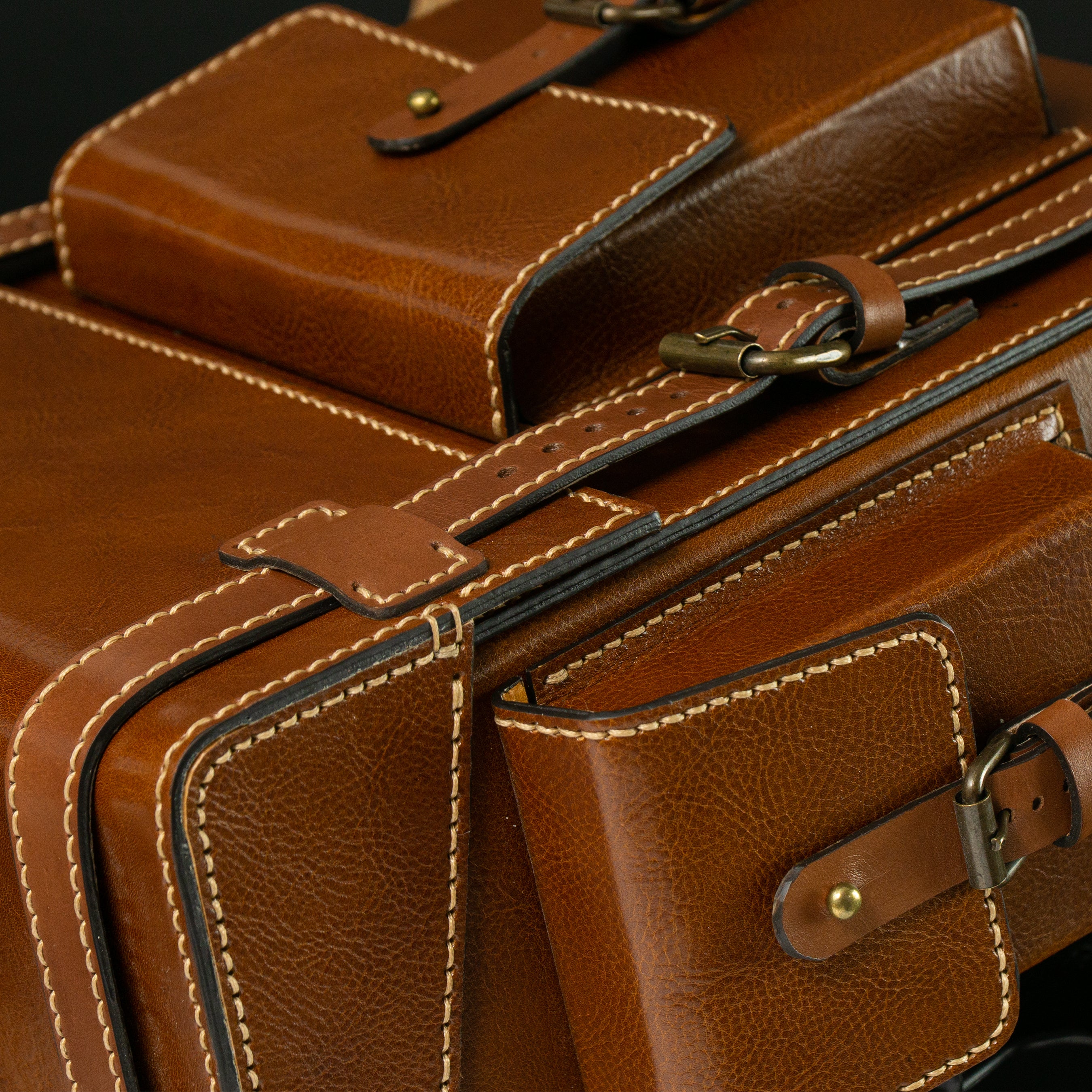 Close-up of a brown leather bag with gold hardware on a dark background.Brown leather Toshiro backpack on a white background, designed and handcrafted by ATOM LEATHER.
