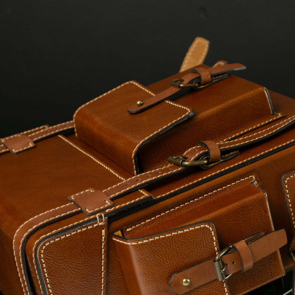 Close-up of a brown leather suitcase with visible stitching details. Brown leather Toshiro backpack on a white background, designed and handcrafted by ATOM LEATHER.