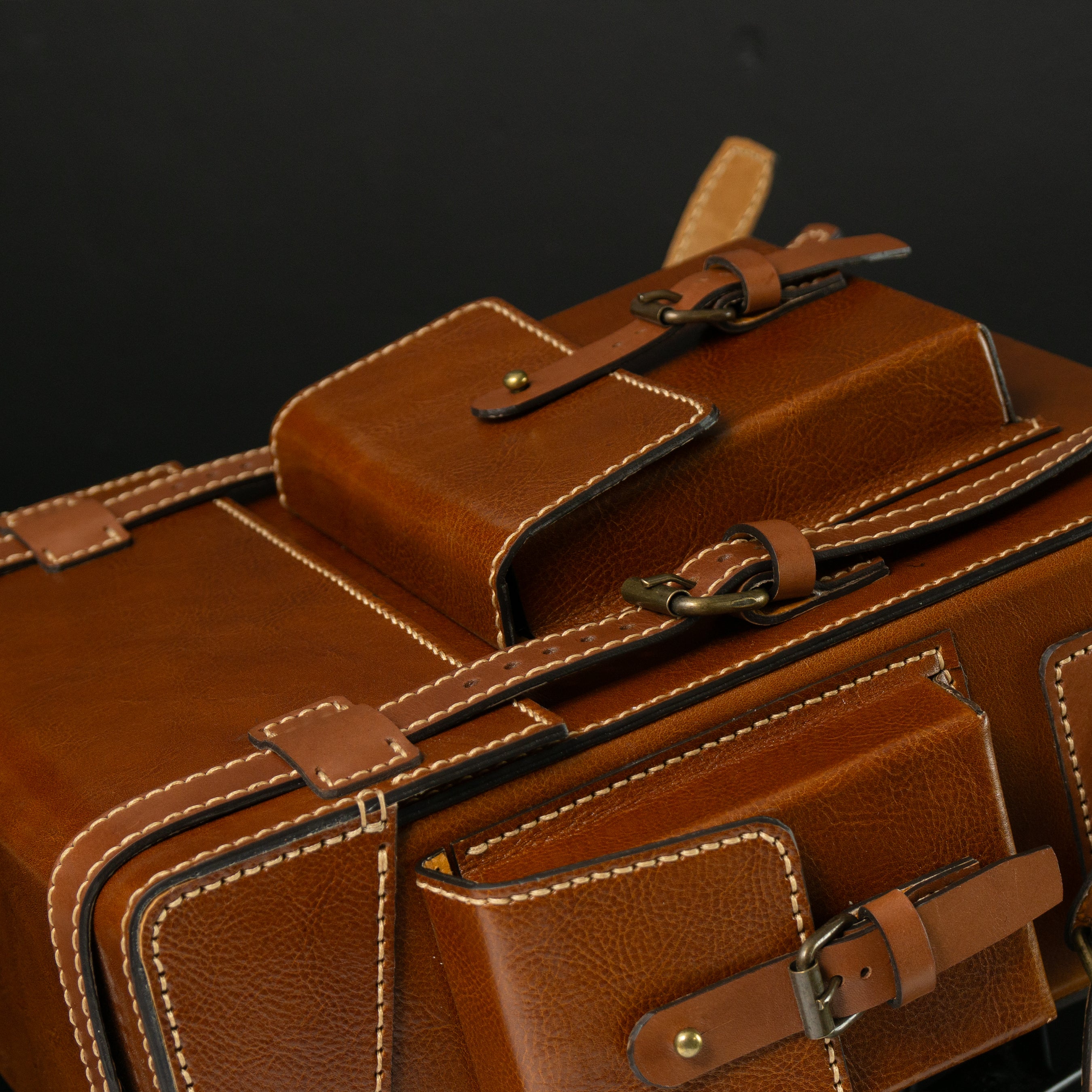 Close-up of a brown leather suitcase with visible stitching details. Brown leather Toshiro backpack on a white background, designed and handcrafted by ATOM LEATHER.